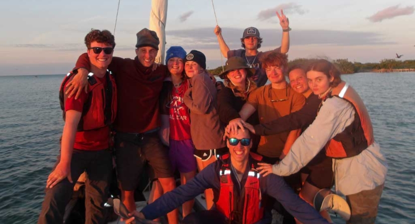 a group of gap year students gather near the shore of a body of water for a group photo